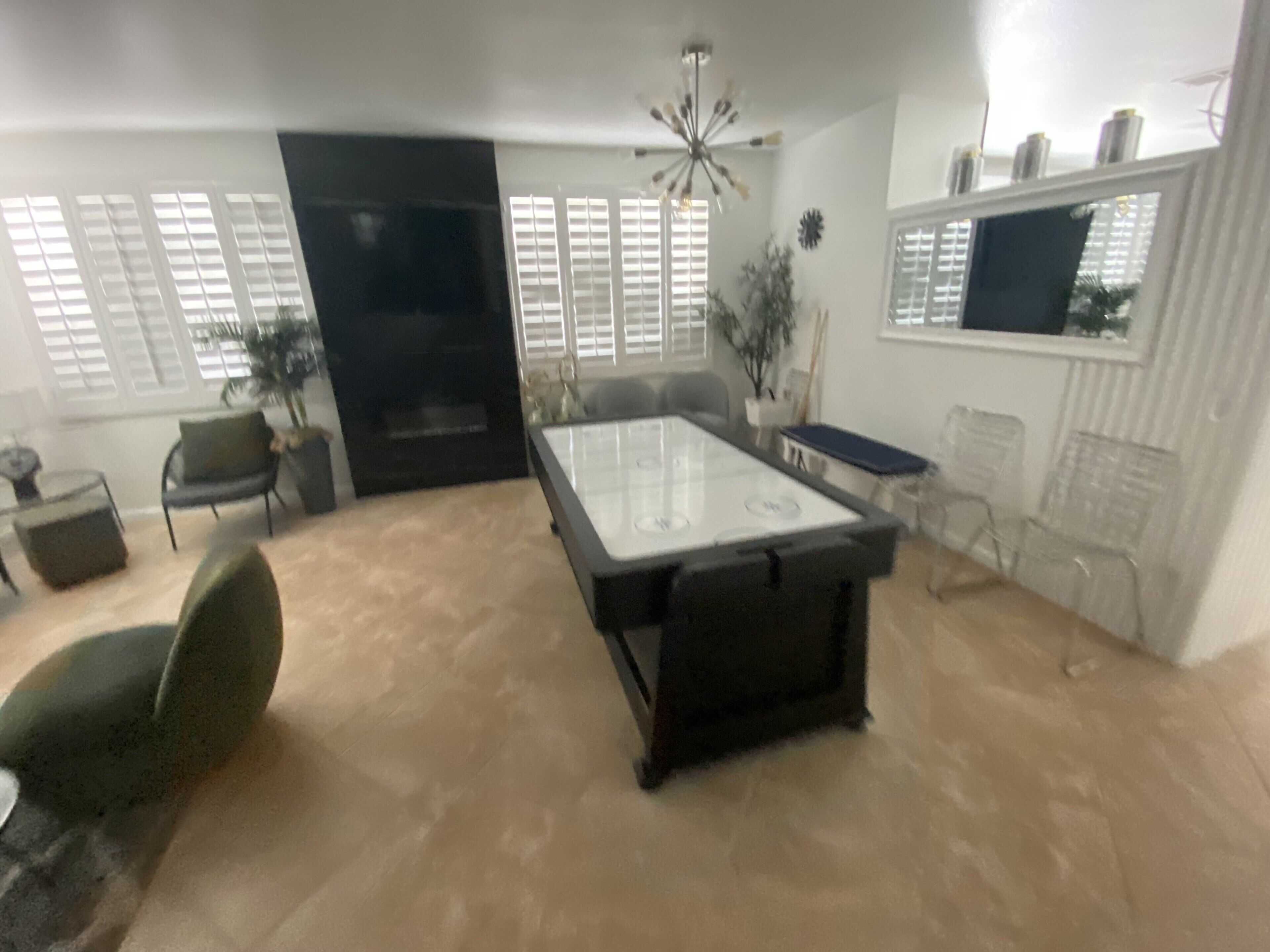 A spacious living room with a billiards table, comfortable seating, and a large window with blinds.