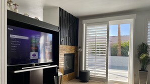 En moderne stue med et fladskærms-tv der viser en Roku-grænseflade, en pejs og en skydedør til en balkon.