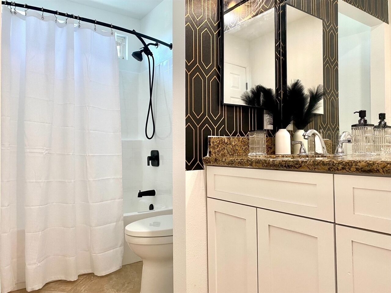 A bathroom with a shower curtain, a toilet, a sink with a mirror, and a patterned wall.