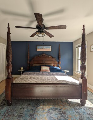 Un letto a baldacchino con testiera in legno, una ventola a soffitto e un quadro con vista sulla città.