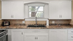 A kitchen with white cabinets, a granite countertop, a built-in sink, and a window above the sink. - Newly Remodeled 3BR in Town · Cherry Street (Van Buren)