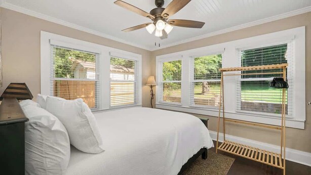 A bedroom with a bed, a ceiling fan, and a window with a wooden rack. - Newly Remodeled 3BR in Town · Cherry Street (Van Buren)