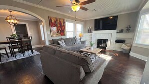 A living room with a dark wood floor, a gray sectional sofa, a dining area with a table and chairs, and a fireplace. - Newly Remodeled 3BR in Town · Cherry Street (Van Buren)
