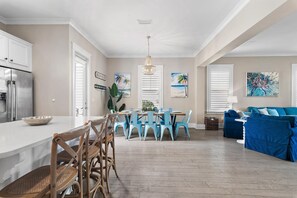 Une cuisine spacieuse dotée d’un îlot central, un coin repas avec des chaises bleues et un salon avec des canapés bleus.