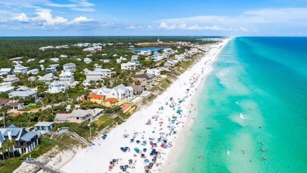 An aerial view of a coastal town with a long sandy beach, numerous beach umbrellas, and a clear blue ocean. - Close to Beach | Golf Cart | Heated Pool (Santa Rosa Beach)