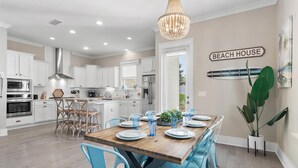 A modern kitchen with white cabinets, a wooden dining table, and blue chairs. - Close to Beach | Golf Cart | Heated Pool (Santa Rosa Beach)