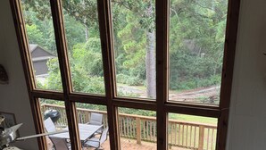 A room with a large window overlooking a deck and a wooded area. There is a brown leather sofa and a wooden table with chairs. - Lakeside cottage, water access + pet friendly with additional fee (Jasper)