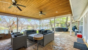 Un patio al aire libre con muebles de mimbre, un ventilador de techo y vistas a un lago.