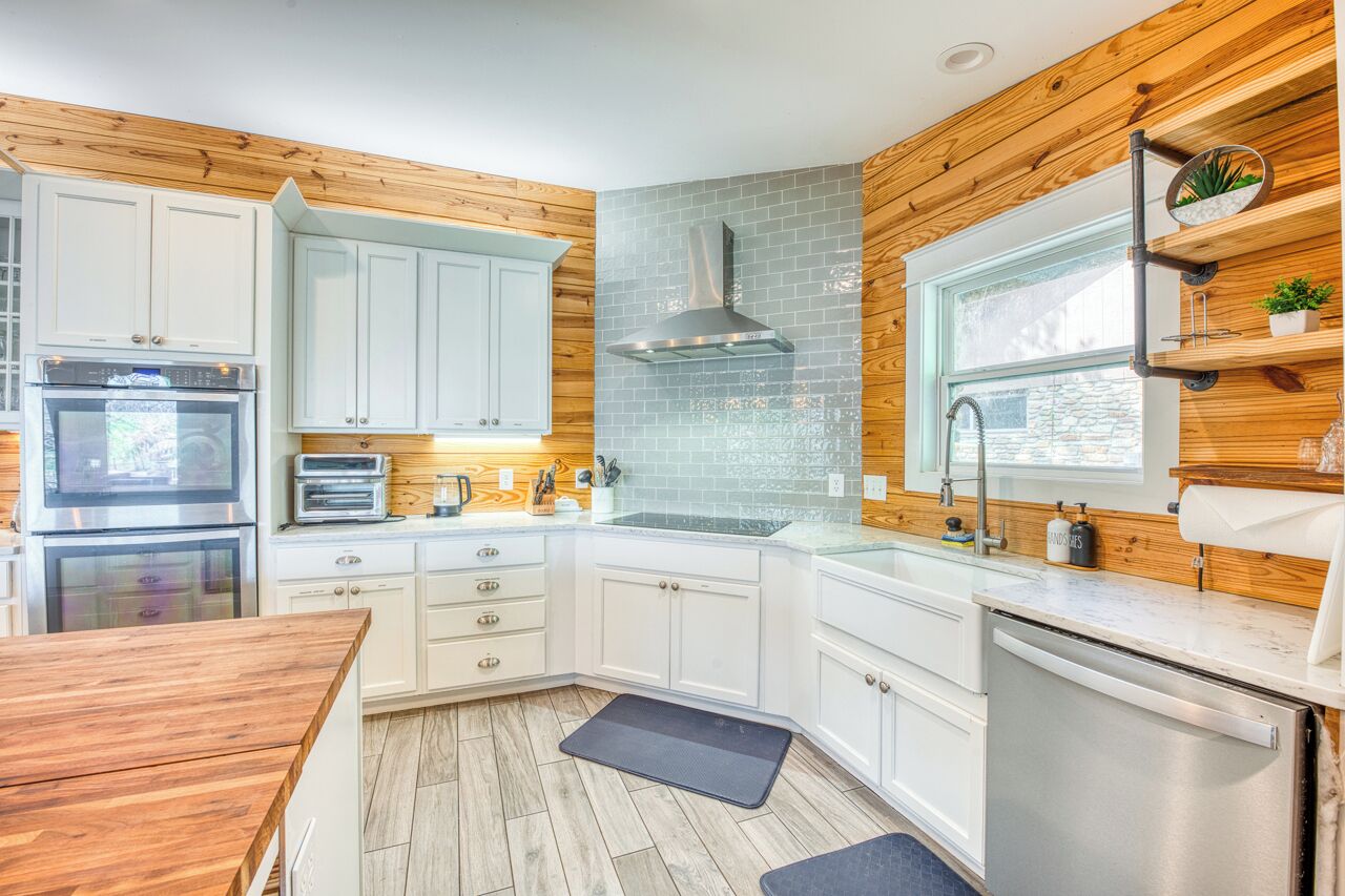 A modern kitchen with white cabinets, a stainless steel range hood, and a window above the sink.