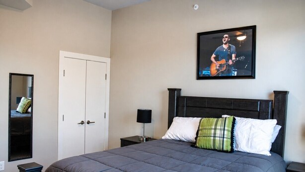 Ein Schlafzimmer mit einem Bett, einem Nachttisch, einer Lampe, einem Spiegel und einem gerahmten Bild an der Wand.