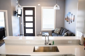 A modern kitchen with a white countertop, stainless steel sink, and pendant lighting.