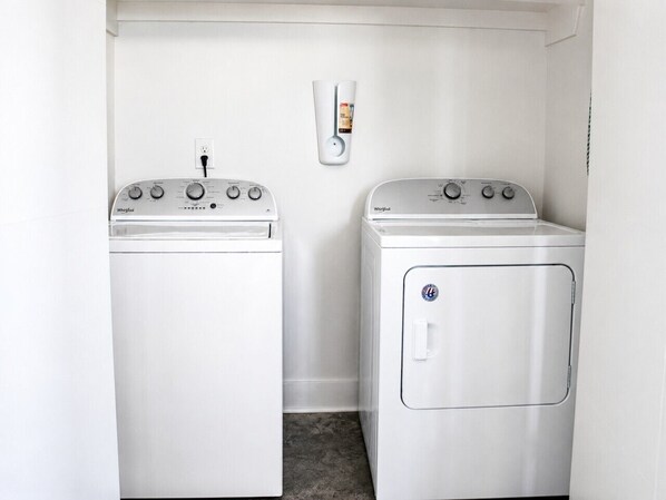 A laundry room with two white Whirlpool washers and a dryer, a wall-mounted soap dispenser, and a power outlet.