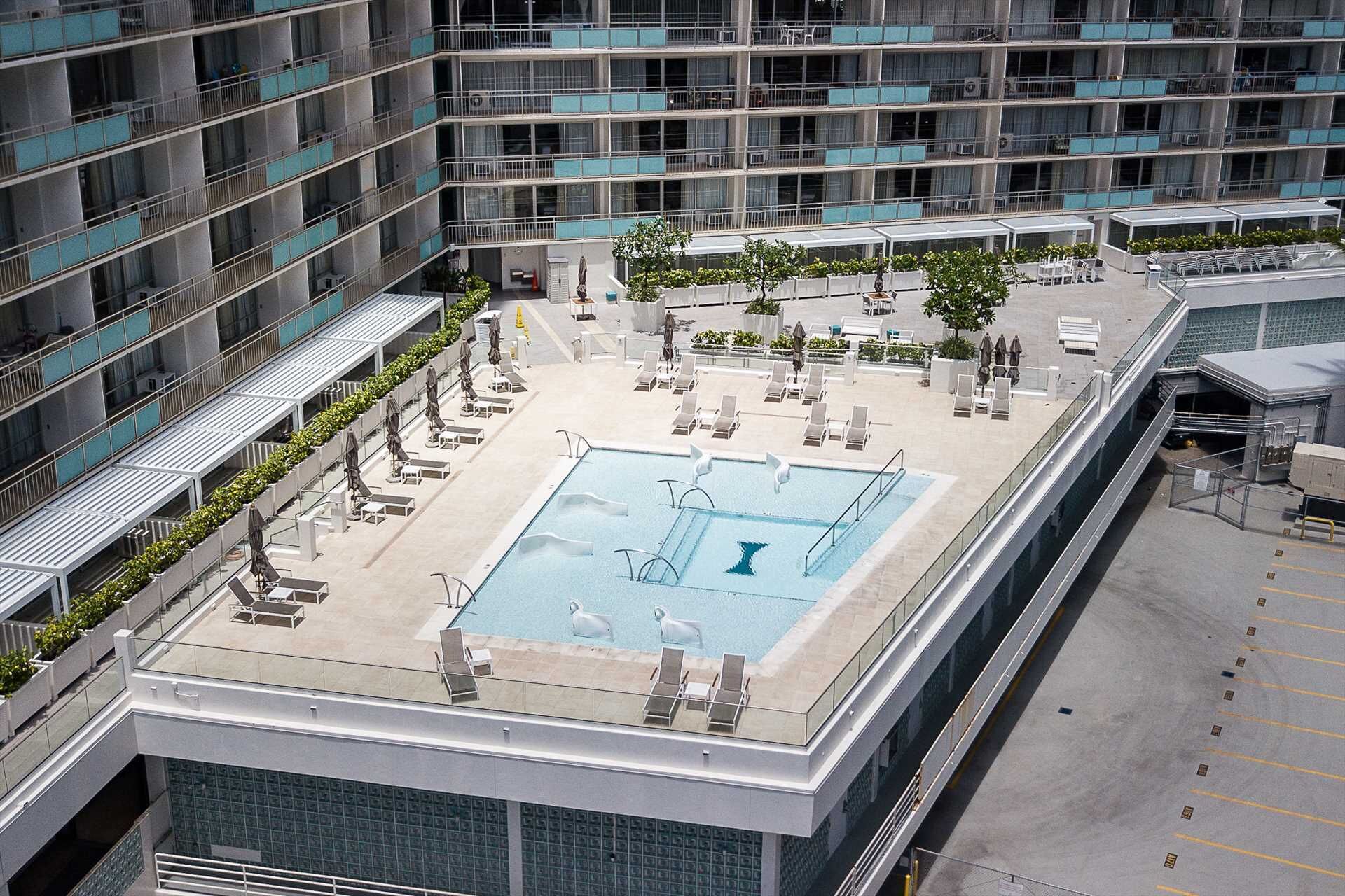 A rooftop pool with lounge chairs and umbrellas, surrounded by a modern building with multiple balconies.