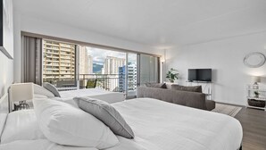 Habitación de hotel moderna con una cama grande, un sofá, un televisor y un balcón con vistas a la ciudad.