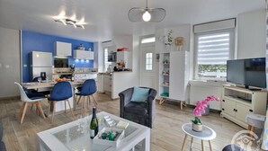 Un salon moderne avec un canapé, une table basse et un téléviseur. Il y a également un coin cuisine avec une table à manger et des chaises.