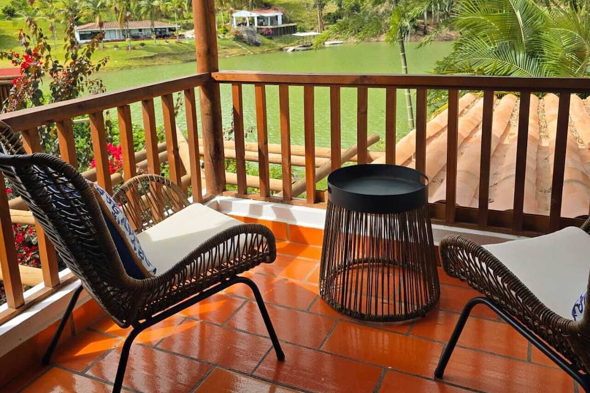 A balcony with wicker chairs and a round table, overlooking a lush landscape with a golf course and distant buildings.