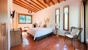Ein Schlafzimmer mit Bett, Nachttisch, Lampe, Stuhl und Blick ins Freie durch ein Fenster.