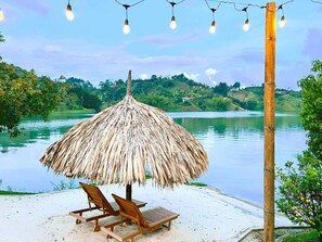 Une plage avec un parasol en chaume et deux chaises en bois.