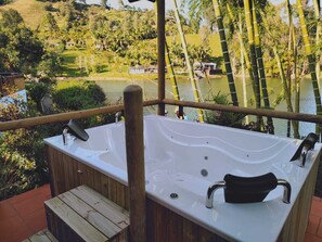 Una terraza de madera con un jacuzzi que da a un lago y un paisaje exuberante.