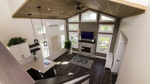 Une cuisine moderne avec une cheminée en pierre, de grandes fenêtres et un plafond en bois.
