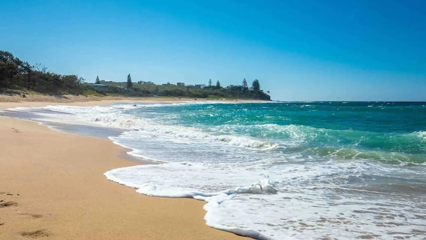 A beach with clear blue waters and a sandy shore.