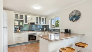 A modern kitchen with white cabinets, a built-in oven, a sink, and a large island with stools.