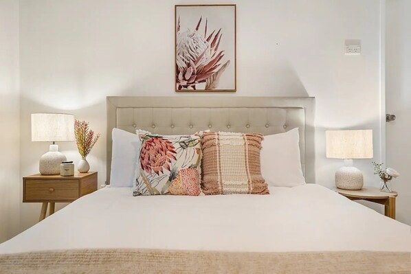A neatly arranged bedroom with a large bed, two bedside tables with lamps, and a framed floral artwork above the bed.