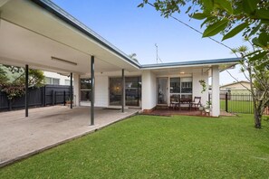 A covered patio area with a dining table and chairs, a small lawn, and a black fence.