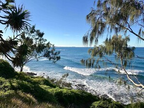 A coastal view with waves, greenery, and a clear sky.