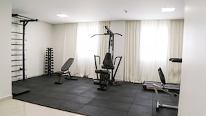 Een fitnessruimte met een optrekstang, gewichtsschijven, een bank, een squatraam en een loopband.