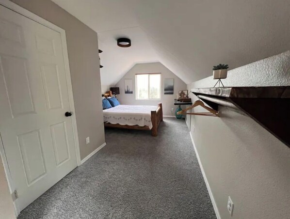 A bedroom with a bed, a window, a door, and a small table with a plant.