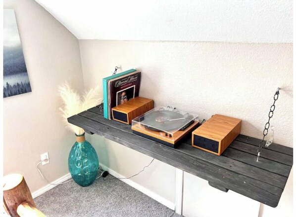 A wooden shelf with a turntable, a small speaker, and a decorative item. - Red Door Cabin (Florissant)
