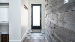A hallway with a wooden wall, a door with a window, and a hexagonal tile floor. - `Bike` at Hills Meaford | 1BD Suite + Pets (Meaford)