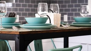 A dining area with teal chairs and matching tableware, a white vase, and a colorful painting on the wall. - `Bike` at Hills Meaford | 1BD Suite + Pets (Meaford)