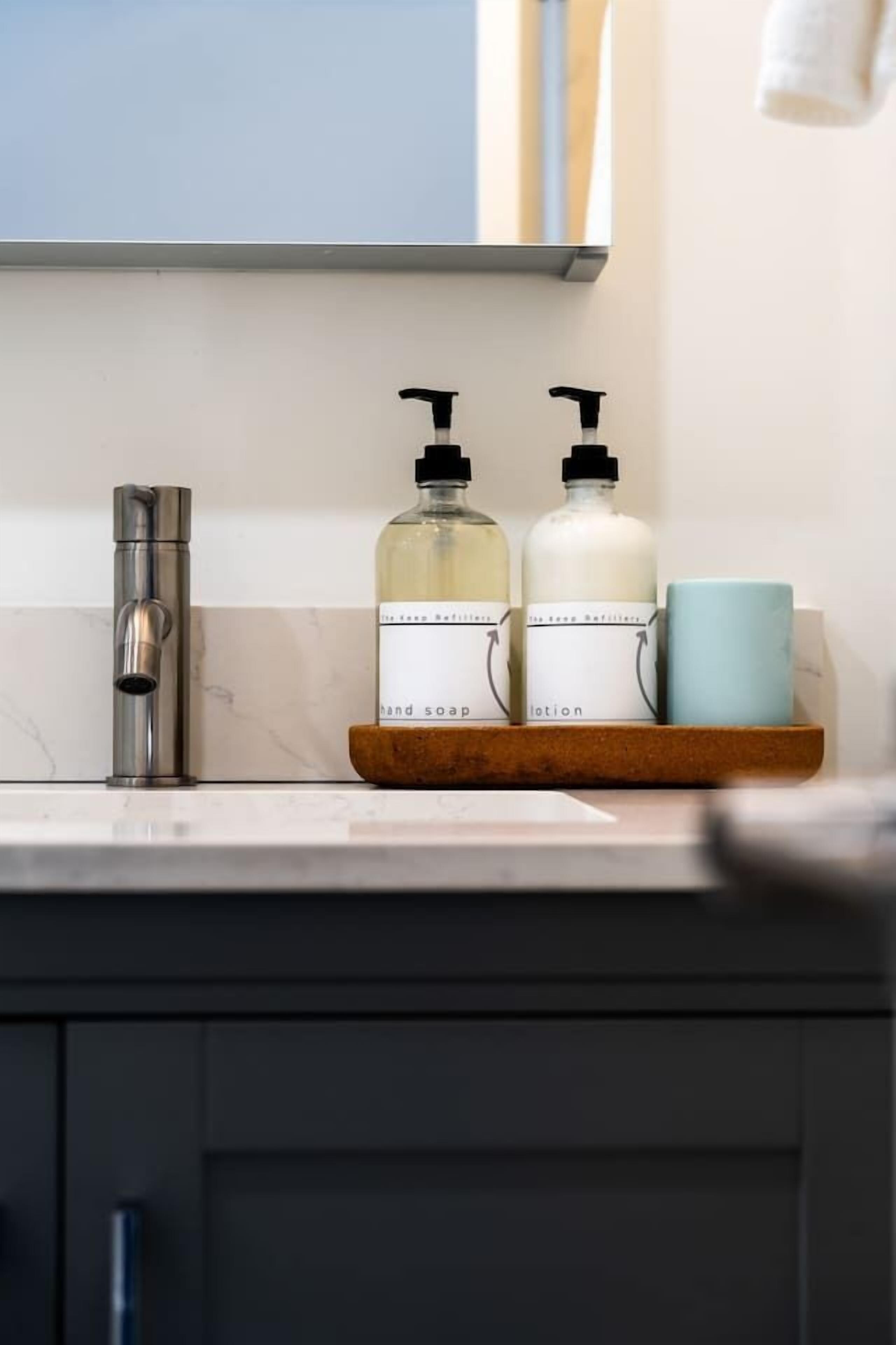 Een badkamer met een moderne kraan, twee zeepdispensers en een blauwe mok op een houten dienblad.