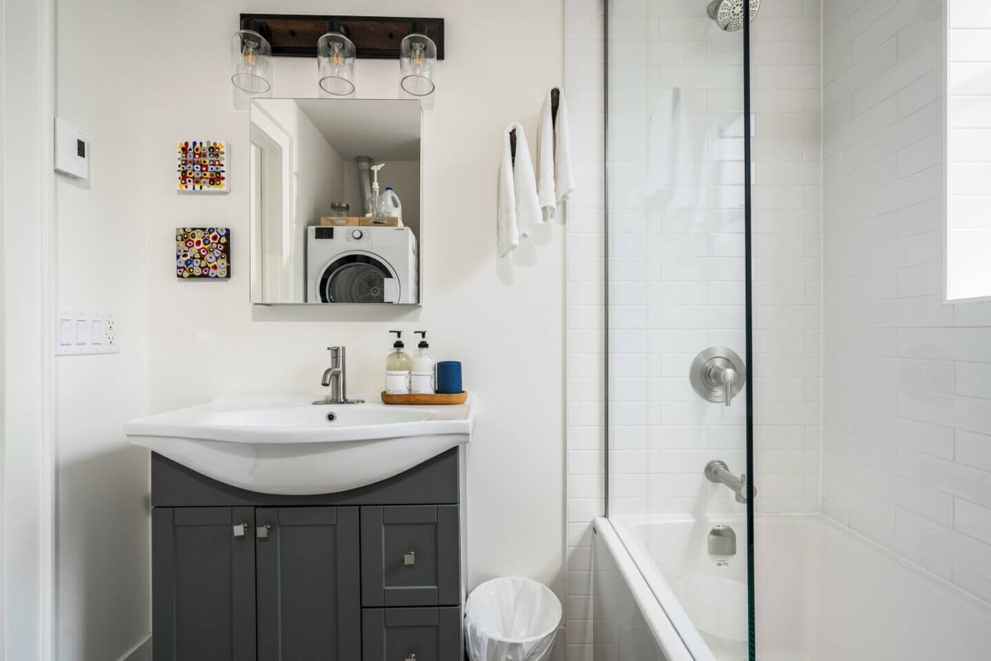 Ein modernes Badezimmer mit einem weißen Waschbecken, dunkelgrauen Schränken, einer Duschkabine aus Glas und einem Spiegel über dem Waschbecken.