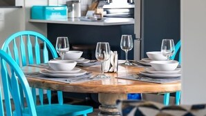 Un comedor con una mesa redonda preparada para cuatro, sillas turquesas y una cocina al fondo.