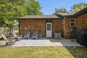 Een stenen huis met een overdekte patio, buitenmeubels en een barbecue.