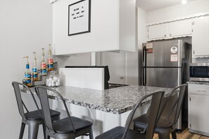 Een keuken met een granieten aanrechtblad, vier barkrukken, een roestvrijstalen koelkast en een bord aan de muur.
