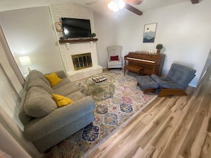 Ein Wohnzimmer mit Sofa, Sessel, Couchtisch, Kamin, Fernseher, Klavier und Teppich.