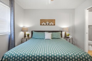 Ein Schlafzimmer mit einem Bett, zwei Nachttischen, einem Wandbild und einem Fenster mit Jalousien.