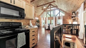 A spacious kitchen with wooden cabinets, a black stove, and a large window. - Sip your coffee in the rocking chairs while enjoying the serene Mountain View’s. (Sevierville)