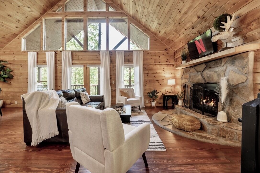 A cozy cabin interior with a stone fireplace, a leather sofa, and a television.