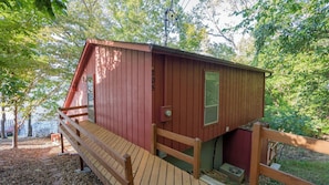 Eine kleine, eingeschossige Holzhütte mit einer Holzterrasse, einer Haustür und einem Fenster.