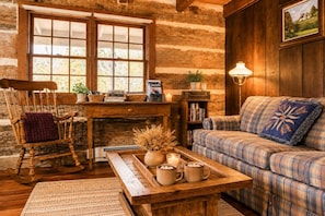 Een landelijk chalet interieur met een houten schommelstoel, een geruite bank, een houten bijzettafeltje met mokken, en een boekenkast.
