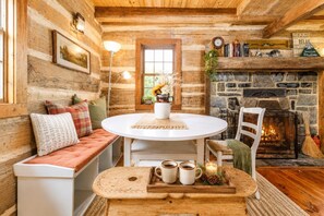 A cozy cabin interior with a stone fireplace, a round dining table, and a seating area with a bench.