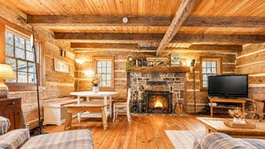 Interior de una cabaña de troncos con chimenea, televisión y mobiliario a cuadros.