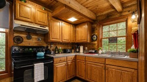 Una cocina con armarios de madera, una estufa negra y una ventana con vistas a la vegetación.