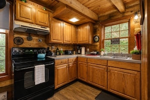 A kitchen with wooden cabinets, a black stove, and a window with a view of greenery.
