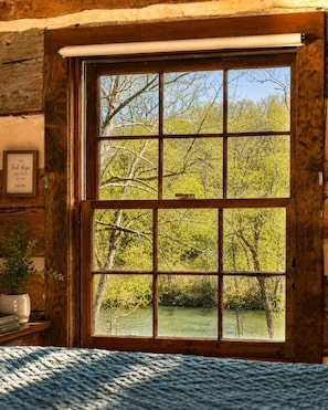 A wooden door with a grid window overlooking a river and trees.
